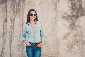 Canvas Print - Portrait of trendy young woman in glasses standing near stone wa