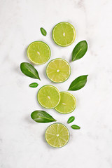 Wall Mural - Juicy lime slices flat lay with green leaves on marble background. Top view