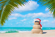 Sandy Snowman in Christmas Santa hat and sunglasses at ocean tropical palm beach