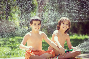 Wall Mural - Cute little boys on summer meadow splashing water having fun and