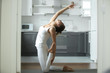 © fizkes - Sporty attractive woman practicing yoga, sitting in Camel exercise, Ustrasana pose , working out, wearing white sportswear, indoor full length, home interior background