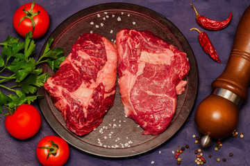 Raw meat. Beef steak on a round cutting board with tomatoes, parsley and spices