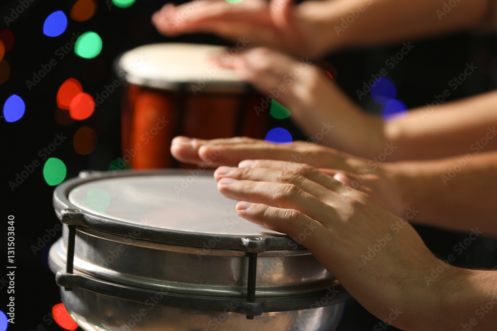 Hands of man playing African drum against defocused lights