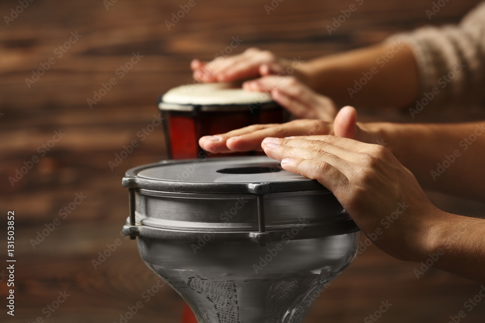 Hands of man playing African drum on brown blurred background