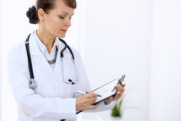 Happy female doctor standing in hospital. Medicine and health care concept.