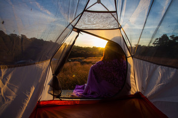 women sit front of camping tent glow up with sunrise in morning