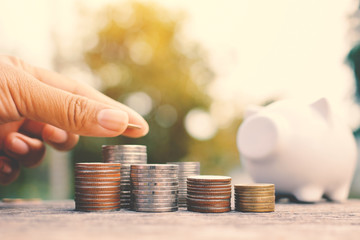 Hand of women holding coin to set money and white piggy bank on old wood background  ,vintage tone