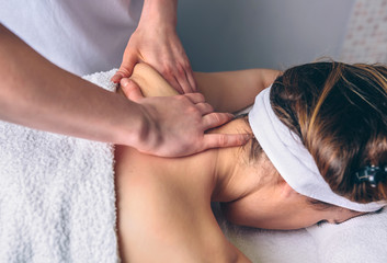 Close up of young woman receiving massage on shoulders in a clinical center. Medicine, healthcare and beauty concept.