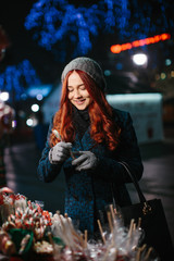 Beautiful young woman buying candy at Christmas market in evening time