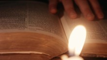 Dolly Shot Of A Man Turning Pages Through An Ancient Book Lit By Candles