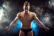 Handsome power athletic man bodybuilder. Fitness muscular body on dark smoke background. Perfect male. Awesome bodybuilder, posing. 