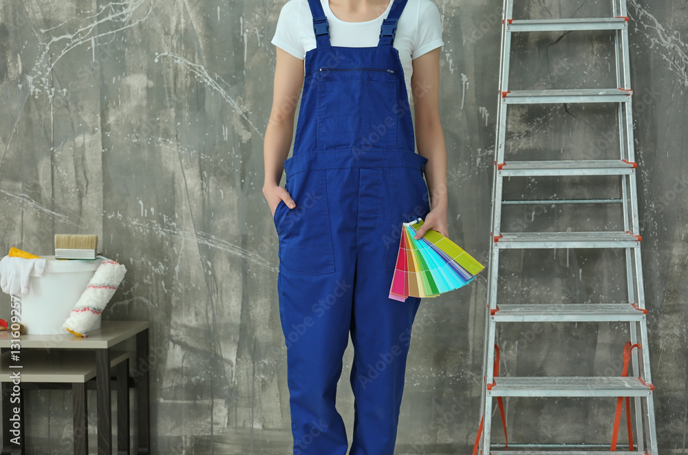 Young female decorator with special tools and ladder near grunge wall