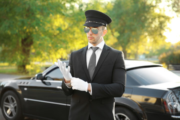 Canvas Print - Young chauffeur adjusting gloves near luxury car on the street