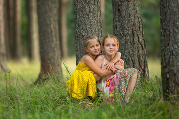 little sisters are sitting near a tree in the park.