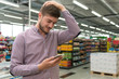 Man Looking Confused At Mobile Phone In Supermarket