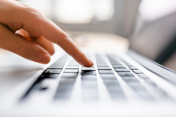 Single finger press button on laptop keyboard, close up clean image with sun flare