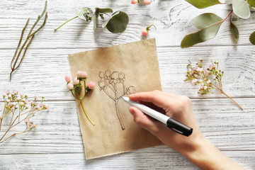 Poster - Female hand drawing flower on paper on white wooden background