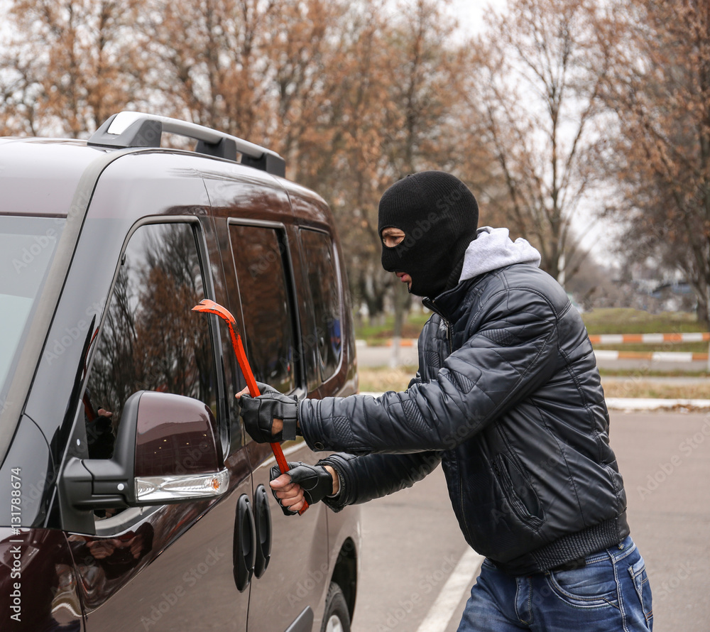 Male thief going to break car window with crowbar