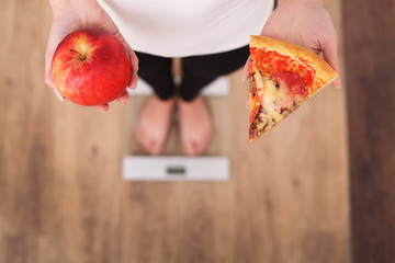 Wall Mural - Diet. Woman Measuring Body Weight On Weighing Scale Holding Pizza. Sweets Are Unhealthy Junk Food. Dieting, Healthy Eating, Lifestyle. Weight Loss. Obesity. Top View