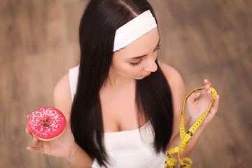 Wall Mural - A young woman holding a donut and a measuring tape. A girl stands on a wooden background. The view from the top. The concept of healthy eating.Diet.