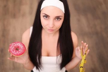Wall Mural - A young woman holding a donut and a measuring tape. A girl stands on a wooden background. The view from the top. The concept of healthy eating.Diet.