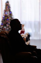 silhouette of a young man on the background of the Christmas tree. Father sad loner in a chair