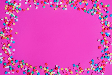 Small star candies on a pink background. Various color sprinkles scattered.

