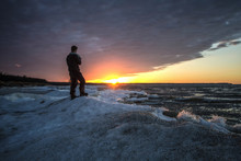 Male Photographer Standing On A Frozen Lake. Single Male Photographer Standing On The Edge Of A Frozen Lake During A Beautiful Winter Sunset. Port Crescent State Park. Port Austin, Michigan.