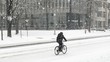 Person Riding Bicycle Through Snow Storm on City Street