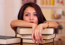 Young Brunette Woman Wearing Pink Top Lying Bent Over Stack Of Books, Tired Facial Expression And Body Language, Student Concept