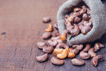 roasted cashew nuts with shell in gunny bag and on wooden background.