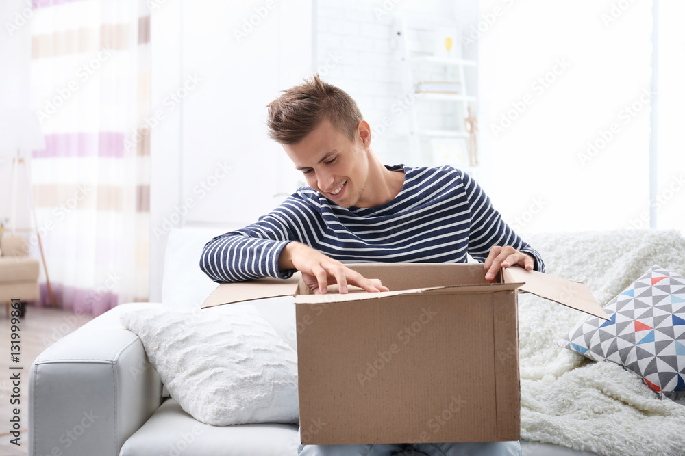 Young man sitting on sofa and unpacking received parcel