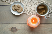 Cozy Home Still Life. Candle Of Pink Salt With Fire, A Cup Of Apple Compote And Plate With Cookies On Knitted Napkin On A Light Wooden Background. Top View.