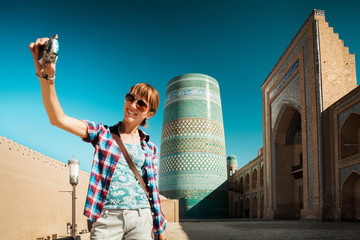 Wall Mural - Young lady taking a selfie with the oriental buildings in Itchan Kala ancient town on the background. Khiva, Uzbekistan