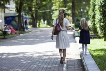 Rear view of young mother walking with little girl daughter in