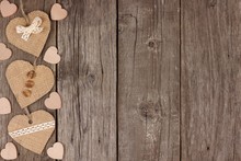 Side Border Of Handmade Burlap Hearts With Ribbon And Buttons Over A Rustic Wooden Background