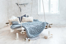 White Loft Interior In Classic Scandinavian Style. Hanging Bed Suspended From The Ceiling. Cozy Large Folded Gray Plaid, Giant Knit Blanket, Super Chunky Yarn, Arm Knitting. Trendy Room Design.
