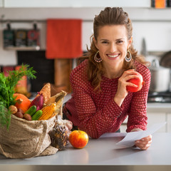 Portrait of happy young housewife holding grocery shopping check