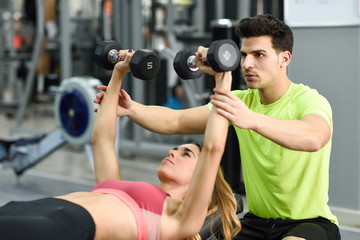 Personal trainer helping a young woman lift weights