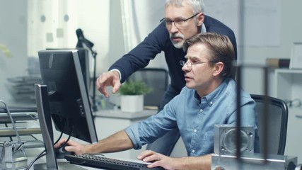 In Busy Engineering Bureau Two Senior Engineers Discussing Technical Issues over Personal Computer. Their Office Looks Minimalistic and Modern.  Shot on RED Cinema Camera in 4K (UHD). 