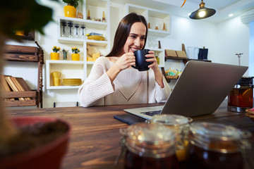 Wall Mural - Delighted woman having a cup of tea while looking at the screen