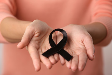 Sticker - Close up view of female hands holding black ribbon. Melanoma and mourning concept