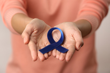 Sticker - Close up view of female hands holding blue ribbon. Colon cancer concept