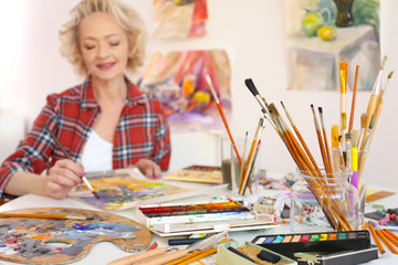 Wall Mural - Different materials and tools on table with senior female artist on background