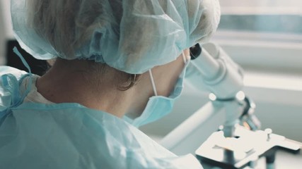Wall Mural - middle age female scientist in uniform and medical face mask doing microscopic examination in labora