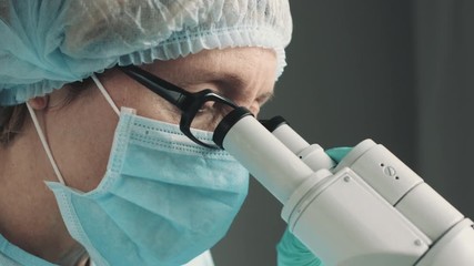 Wall Mural - middle age female scientist in uniform and medical face mask doing microscopic examination in labora
