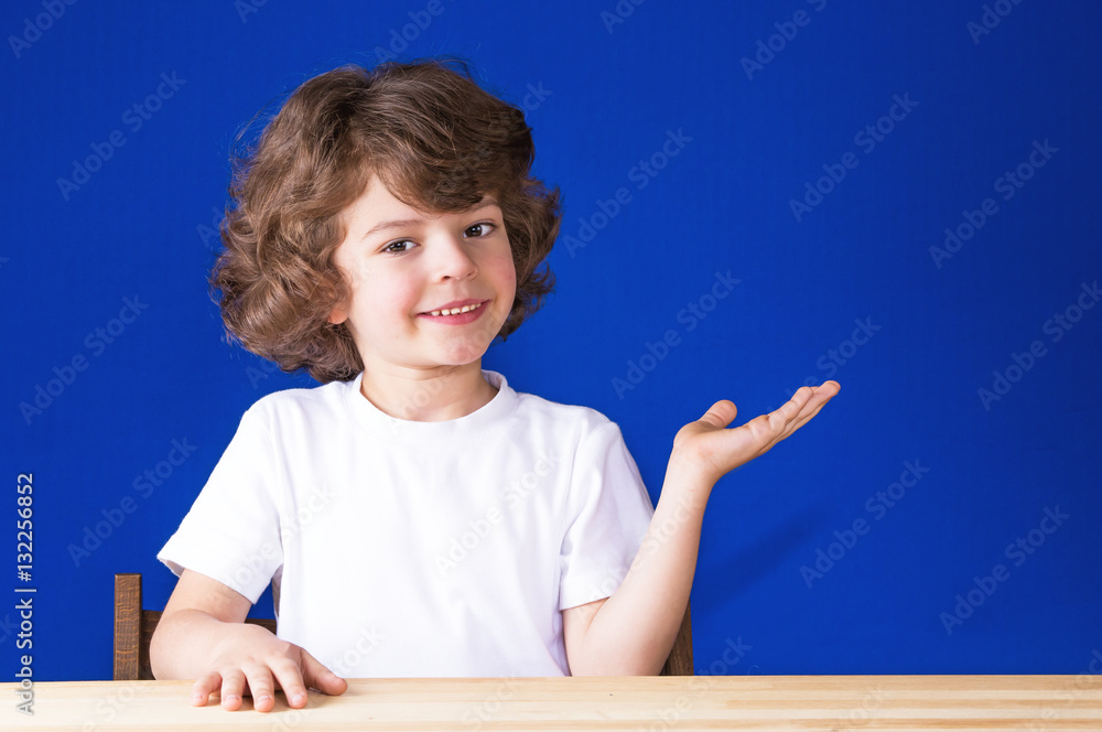Curly cute boy raising his left hand palm up with a smile, looking into ...