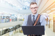 © whyframeshot - Young handsome businessman standing with laptop in the big city