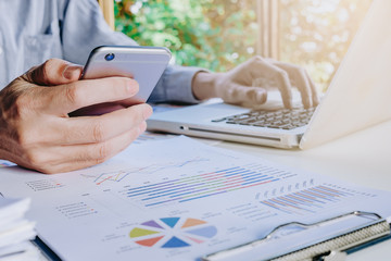 Businessman working with smart phone and discussing the analysis charts or graphs on modern White office desk table .Close up business team analysis and strategy concept with sun flare.