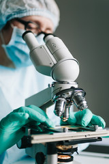 Wall Mural - scientist in blue medical gloves and uniform learning samples with microscope in laboratory.